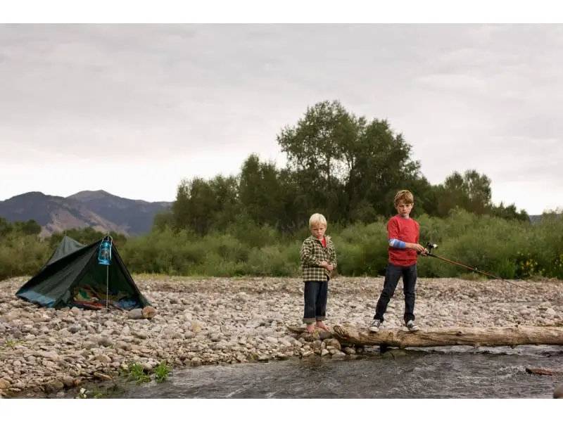 a tent is set up near river while two children staring the water of river