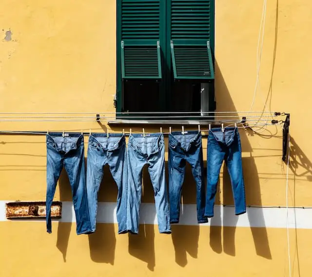 Several pairs of jeans are hanged on a rope to dry, the jeans look shrunk and have wrinkles