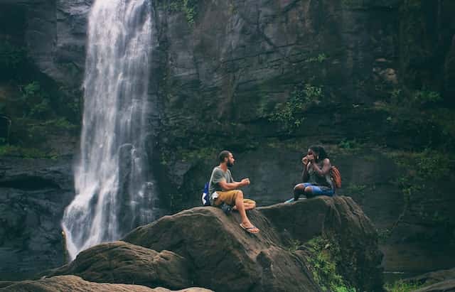 couples sitting near a waterfall during adventure camping