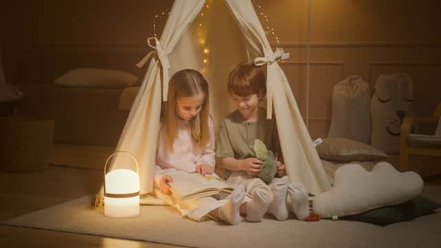 two childs are sitting inside a custom made baby tent inside the living room to create the camping experience