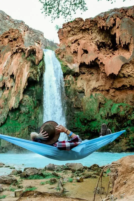 man laying on blue hammock in front of waterfall