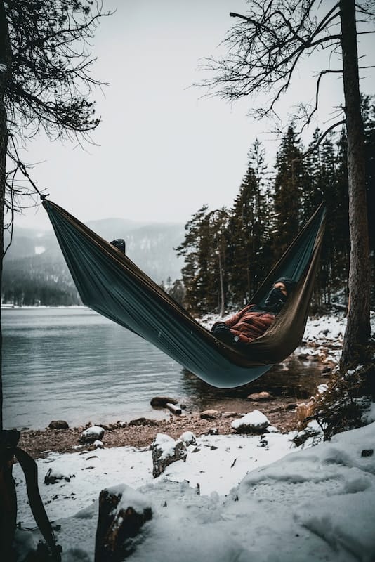 a person laying in a hammock by a lake in winter