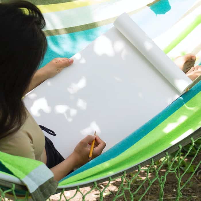 a woman sitting in a hammock writing on a piece of paper